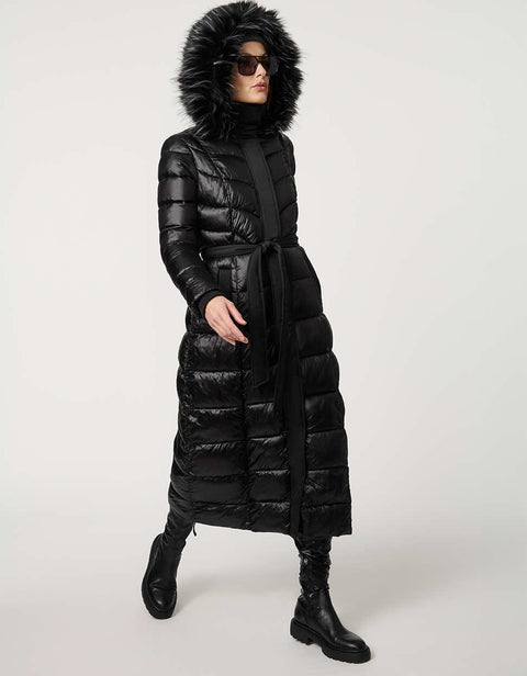 Person wearing a long black puffer coat with a fur-lined hood on a white background