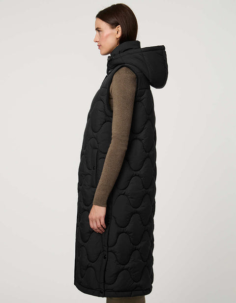A woman shown from the side in a long black puffer vest with a detachable hood.