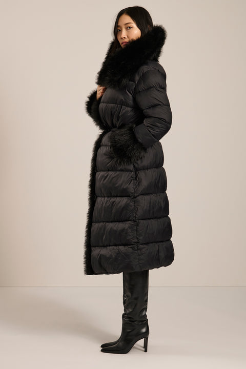 The profile of a woman in a long black puffer coat with a faux fur shawl collar.