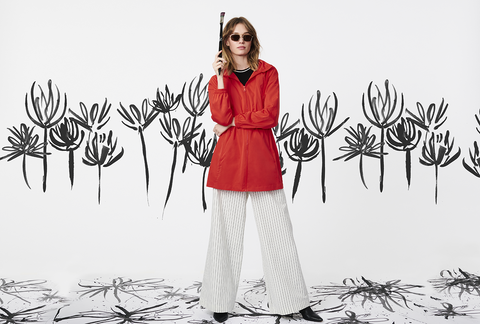 A spring outerwear model in sunglasses with a paintbrush in front of a canvas.