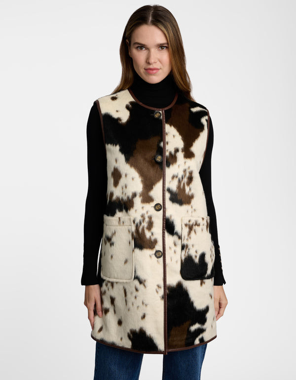 A woman in a long, sleeveless cow print vest with patch pockets and button closures.