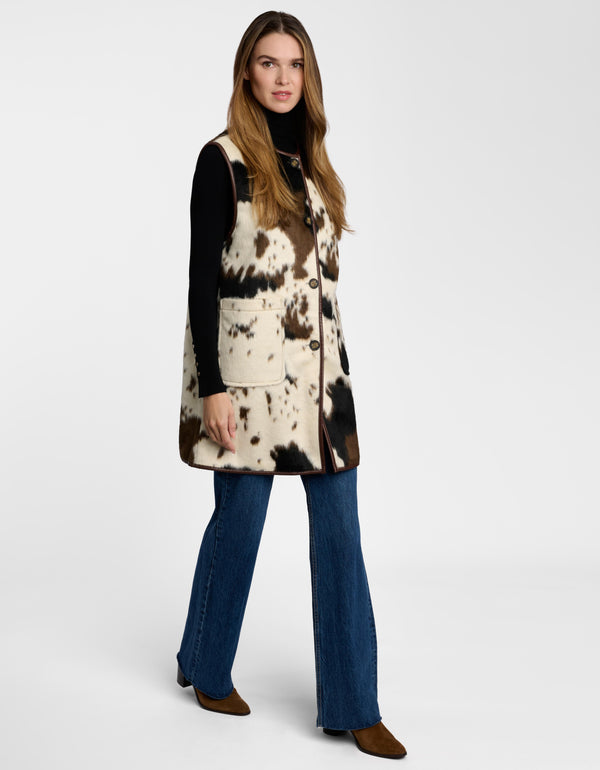 A model wearing a women's cow print vest styled over a turtleneck.