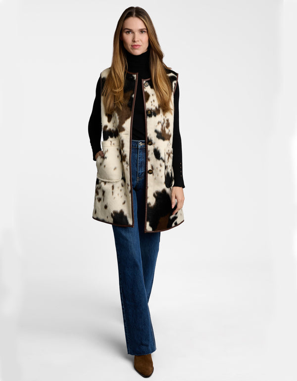 A model in a faux fur cow print vest for women with patch pockets and button closures.