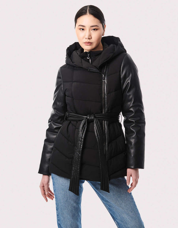 A women's belted puffer jacket with vegan leather sleeves, asymmetrical zipper, and zip-off hood for versatile styling.