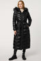 A female model wearing a long vegan puffer coat with a fur-lined hood on a white background