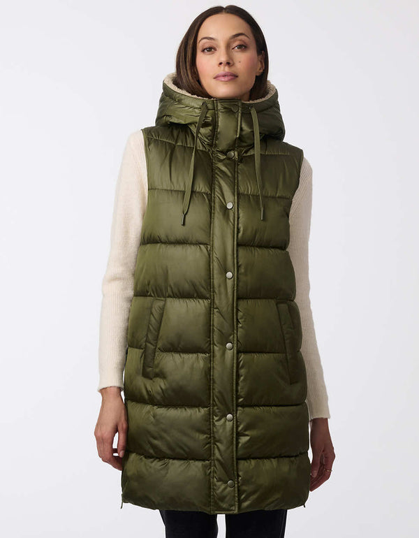 womens thigh-length insulated vest with sherpa-lined hood and modern horizontal stitching. Made with recycled insulation. Combines coziness with contemporary design for cold-weather layering.