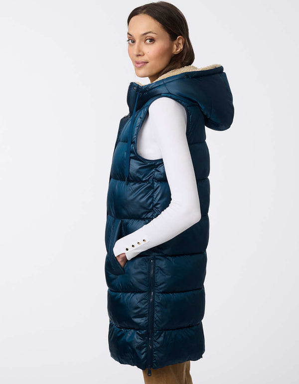 womens thigh-length insulated vest with sherpa-lined hood and modern horizontal stitching. Made with recycled insulation. Combines coziness with contemporary design for cold-weather layering.