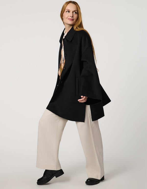 Modern women’s wool poncho coat with draped silhouette, side slits, structured collar, and welt pockets.