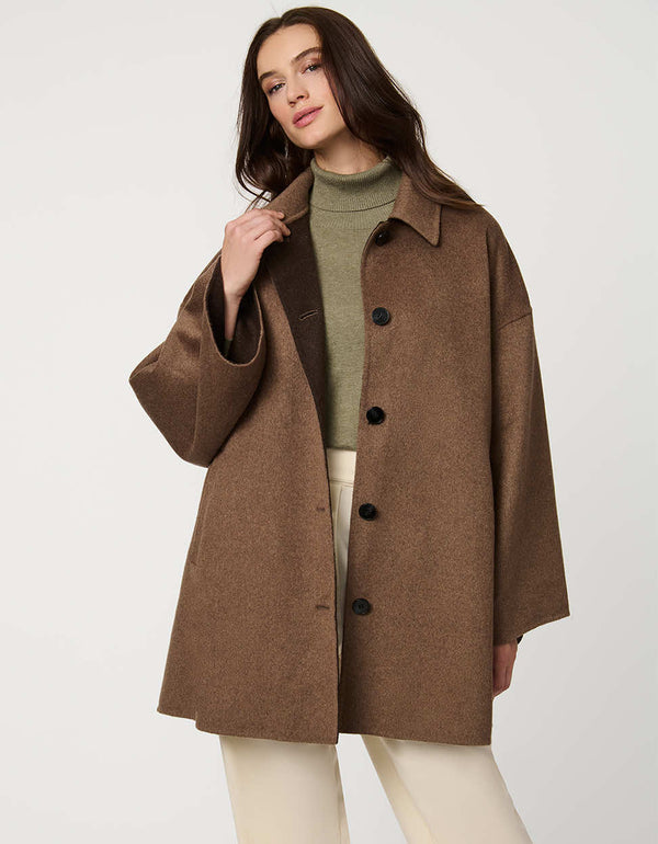 Modern women’s wool poncho coat with draped silhouette, side slits, structured collar, and welt pockets.
