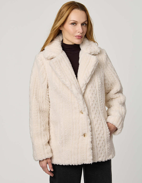 Woman wearing a cream fur coat against a plain background