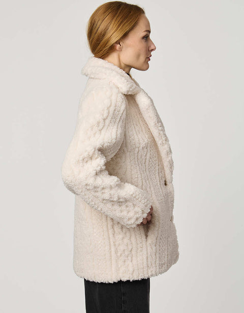 Woman wearing a cream-colored knitted jacket on a plain background
