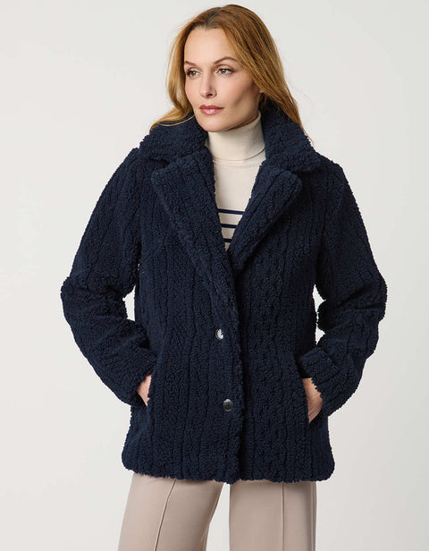Woman wearing a navy blue coat, striped sweater, and beige pants on a white background