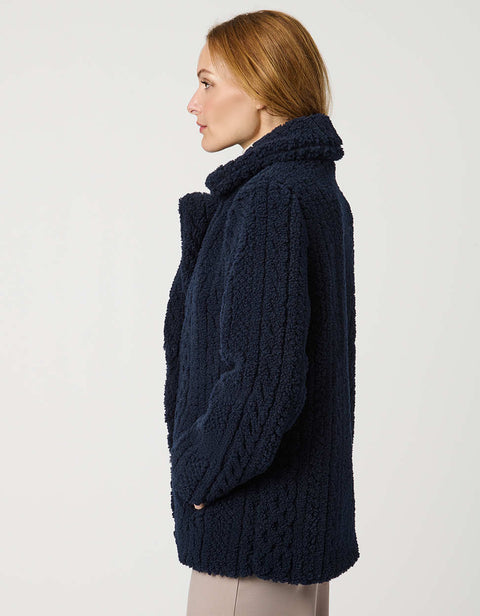 Woman wearing a navy blue coat, striped sweater, and beige pants on a white background