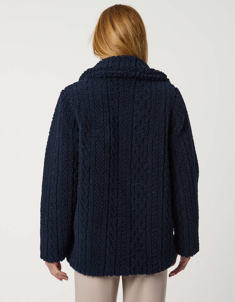 Woman wearing a navy blue coat, striped sweater, and beige pants on a white background