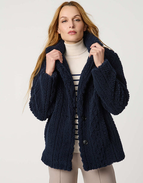 Woman wearing a navy blue coat, striped sweater, and beige pants on a white background