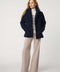 Woman wearing a navy blue coat, striped sweater, and beige pants on a white background