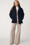 Woman wearing a navy blue coat, striped sweater, and beige pants on a white background