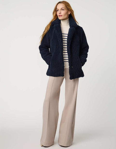 Woman wearing a navy blue coat, striped sweater, and beige pants on a white background