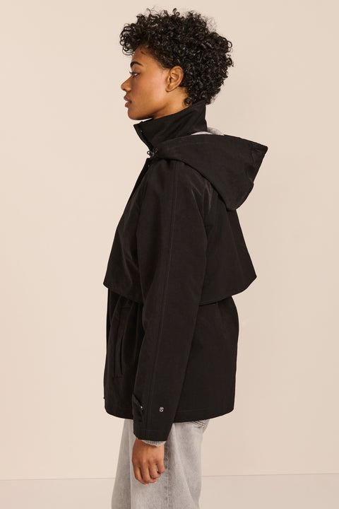 Women's hooded raincoat with drawstring waist, storm flap, side pockets and adjustable cuffs.