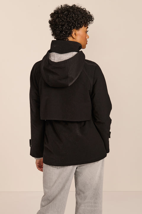 Women's hooded raincoat with drawstring waist, storm flap, side pockets and adjustable cuffs.