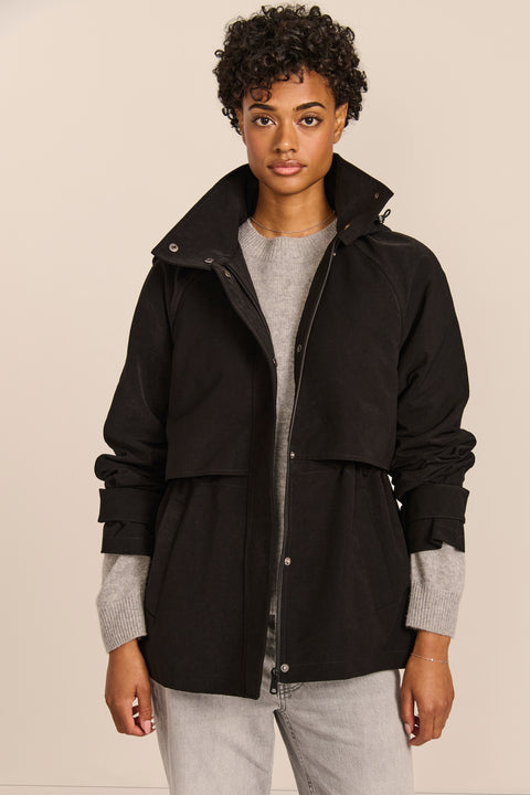 Women's hooded raincoat with drawstring waist, storm flap, side pockets and adjustable cuffs.