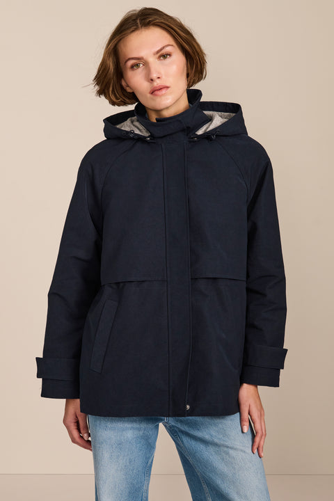 Women's hooded raincoat with drawstring waist, storm flap, side pockets and adjustable cuffs.