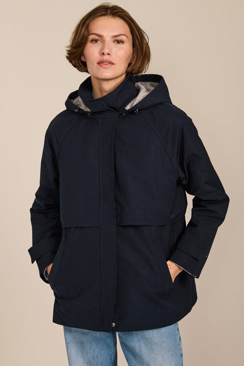 Women's hooded raincoat with drawstring waist, storm flap, side pockets and adjustable cuffs.