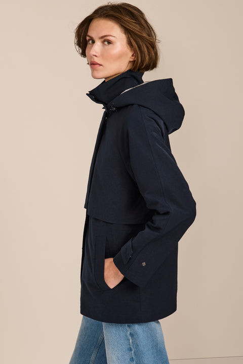 Women's hooded raincoat with drawstring waist, storm flap, side pockets and adjustable cuffs.
