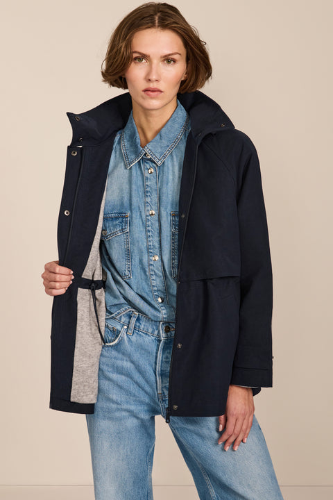 Women's hooded raincoat with drawstring waist, storm flap, side pockets and adjustable cuffs.