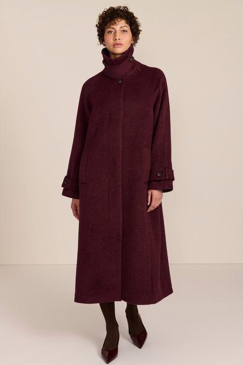 Women's long wool coat featuring a sculptural stand collar, concealed front closure, patch pockets, and button-tab cuffs.