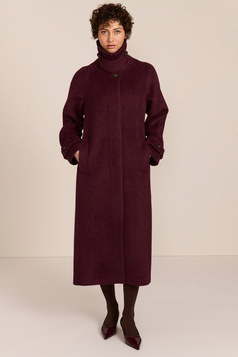 Women's long wool coat featuring a sculptural stand collar, concealed front closure, patch pockets, and button-tab cuffs.