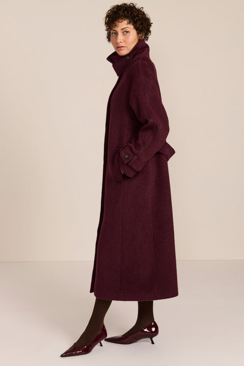 Women's long wool coat featuring a sculptural stand collar, concealed front closure, patch pockets, and button-tab cuffs.