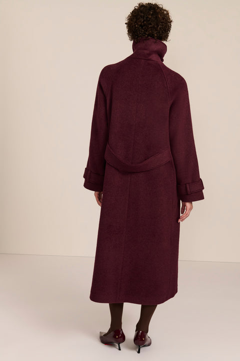 Women's long wool coat featuring a sculptural stand collar, concealed front closure, patch pockets, and button-tab cuffs.