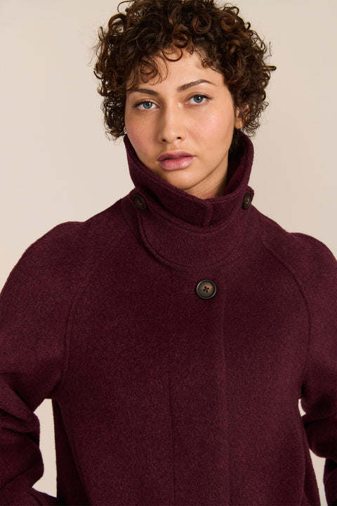 Women's long wool coat featuring a sculptural stand collar, concealed front closure, patch pockets, and button-tab cuffs.