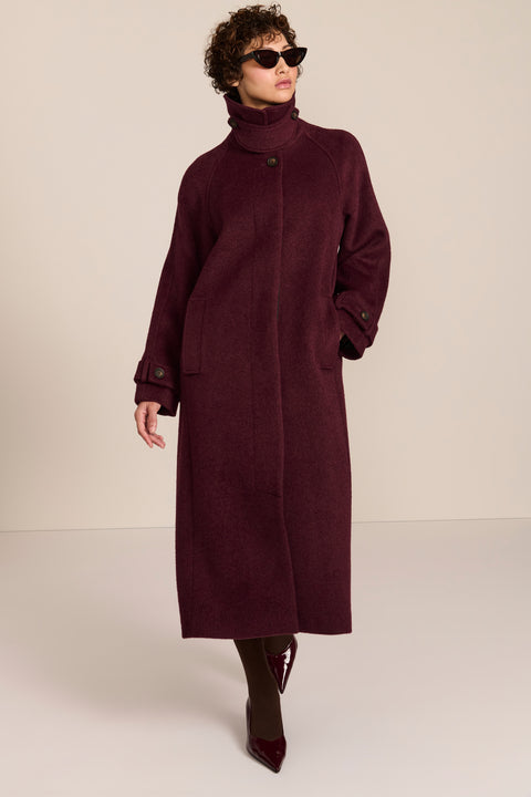 Women's long wool coat featuring a sculptural stand collar, concealed front closure, patch pockets, and button-tab cuffs.