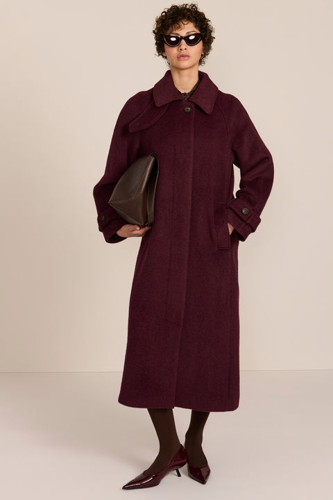 Women's long wool coat featuring a sculptural stand collar, concealed front closure, patch pockets, and button-tab cuffs.