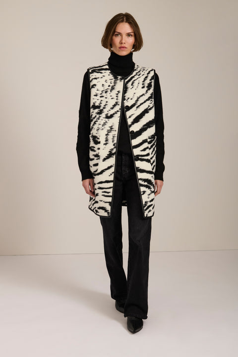 Long Bengal-inspired faux fur vest with collarless silhouette, faux leather trim and elongated fit.