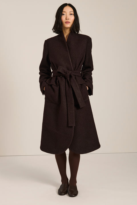 Belted bouclé wrap coat with rounded shawl collar, textured fabric and modern wrap silhouette.