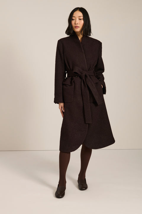 Belted bouclé wrap coat with rounded shawl collar, textured fabric and modern wrap silhouette.