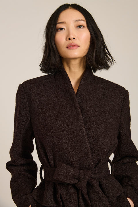 Belted bouclé wrap coat with rounded shawl collar, textured fabric and modern wrap silhouette.