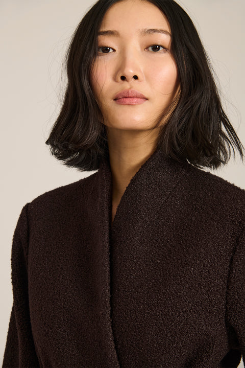 Belted bouclé wrap coat with rounded shawl collar, textured fabric and modern wrap silhouette.