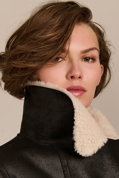 women's black faux shearling belted coat featuring ivory contrast trim, oversized notched collar, zip-front closure and zip pockets.