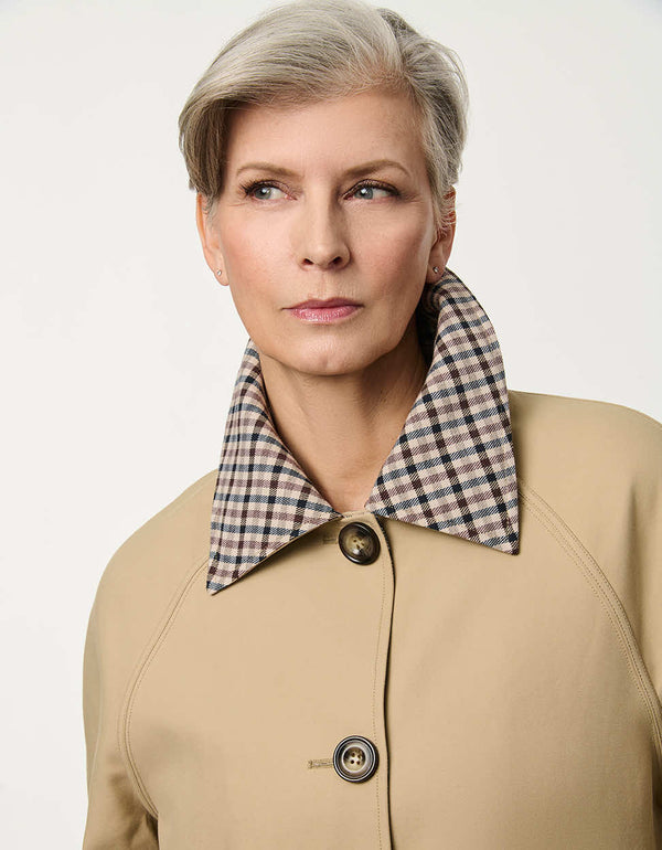 Women’s khaki trench coat with a streamlined silhouette, button front, side pockets, and contrasting plaid collar.
