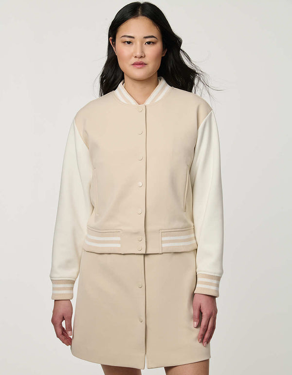 Woman wearing neutral Modern Varsity Jacket with contrast sleeves, ribbed trim, snap-front closure and welt pockets.