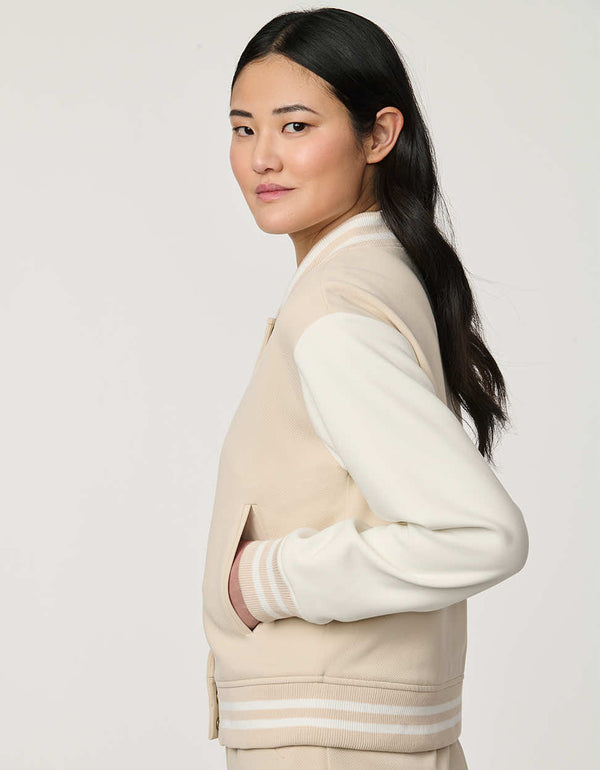 Woman wearing neutral Modern Varsity Jacket with contrast sleeves, ribbed trim, snap-front closure and welt pockets.