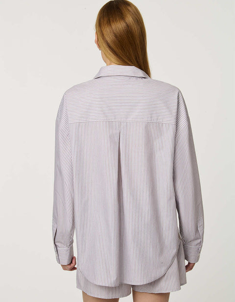 Woman wearing oversized Striped Poplin Boyfriend Shirt with button front and vertical side stripe.