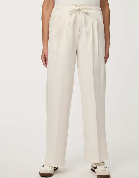 Woman wearing cream white pleated drawstring trousers with elastic waist and straight-leg silhouette.