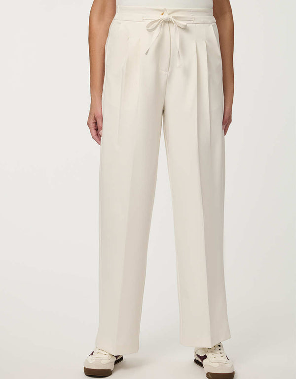 Woman wearing cream white pleated drawstring trousers with elastic waist and straight-leg silhouette.