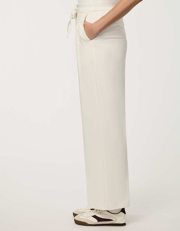Woman wearing cream white pleated drawstring trousers with elastic waist and straight-leg silhouette.