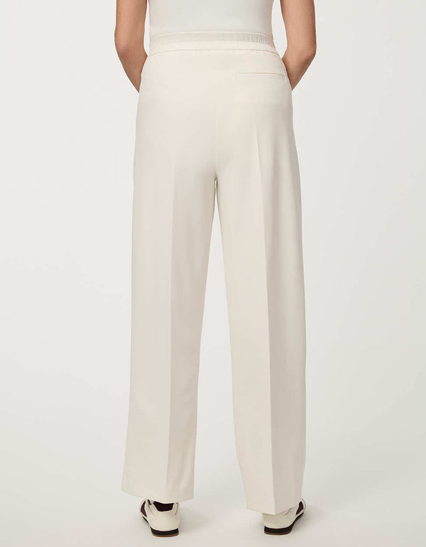 Woman wearing cream white pleated drawstring trousers with elastic waist and straight-leg silhouette.